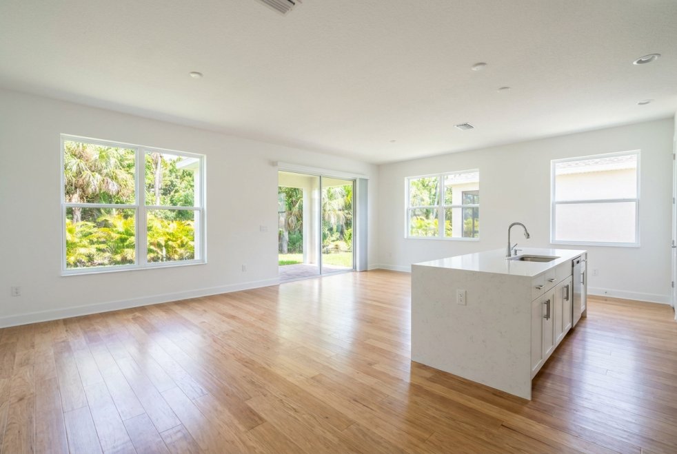 Clean empty home interior with hardwood floors, kitchen island, and large windows